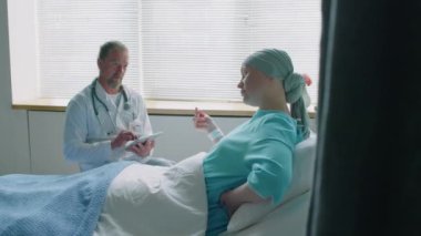 Kanserli genç bir kadının hastane koğuşunda yatarken doktorla iletişim kurduğu orta boy bir fotoğraf.