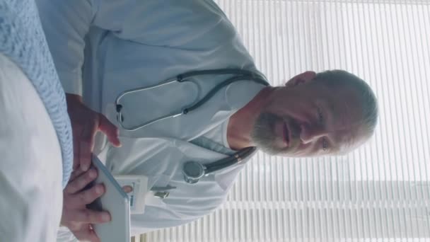 Pionowe Ujęcie Dojrzałego Lekarza Cyfrową Tabletką Rękach Pytającego Pacjenta Objawy — Wideo stockowe