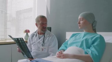 Yetişkin bir doktorun, genç üzgün kanser hastasıyla tartıştığı bir fotoğraf. MRI sonuçları hastane odasında yan yana otururken geldi.