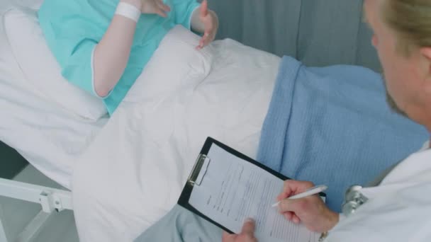 Hochwinkelaufnahme Des Arztes Beim Ausfüllen Der Gesundheitskarte Einer Jungen Krebspatientin — Stockvideo
