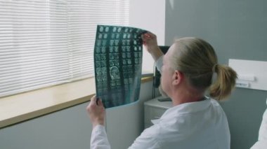 Olgun onkolojistin MRI görüntüsüne bakarken ve yatakta bir kadınla pozitif sonuç hakkında konuşurken orta boy fotoğrafı.