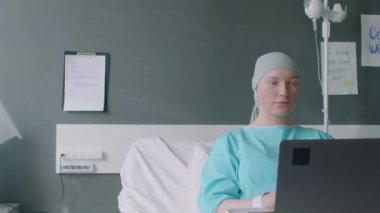 Kanser hastası genç bir kadının hastanenin koğuşunda yatarken arkadaşlarını laptoptan ararken orta boy fotoğrafı.