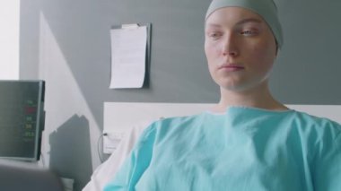 Onkoloji hastanesinin koğuşunda yatarken dizüstü bilgisayar kullanan kanserli genç bir kadın.