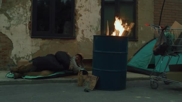 男人睡在街边火桶旁边喝啤酒的镜头很长 — 图库视频影像