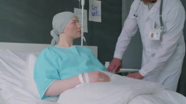 Beyaz önlüklü olgun bir doktor hastanenin koğuşunda kanser olan genç bayan hastalar için kemoterapi için tıbbi damlalar hazırlıyor.
