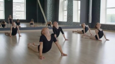 Jimnastik stüdyosunda sırtüstü uzanan küçük kızlar grubunun uzun bir çekimi.