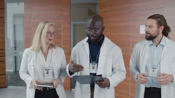 近代的な診療所のホールを歩き 何かを議論する医師の多民族チーム — ストック動画