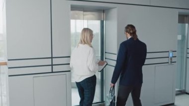 İş arkadaşlarının modern binada asansöre binip konuştuğu orta boy bir fotoğraf.