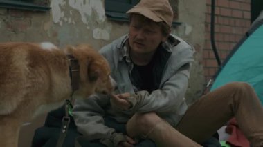 Terk edilmiş bir bölgede sokak ortasında köpeğini besleyen bir dilenci resmi.