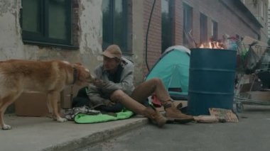 Evsiz bir adamın sokakta otururken köpeğine yemek yedirdiği orta boy bir fotoğraf.