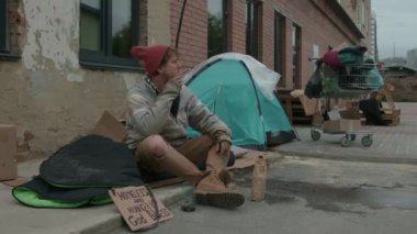 Kendi kendini yapmış bir barınağın yanında sigara içen orta boy bir berduş fotoğrafı.