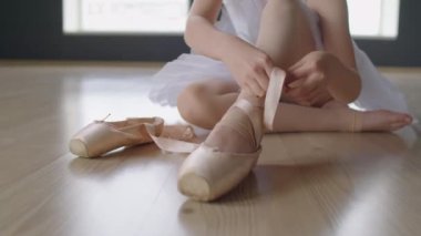 Stüdyoda, bale dersine hazırlanırken ipek kurdele takan bir kızın çekimleri.