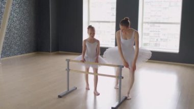 Tutu giymiş genç bir bayan eğitmenin, büyük bir stüdyoda, küçük bir bale dansçısına ihtiyaç duyulan pozun nasıl verileceğini öğretmesi.