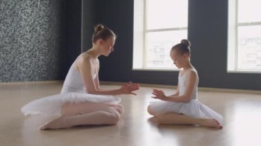 Genç eğitmenin stüdyoda yerde otururken küçük balerinin parmaklarını doğru pozisyonda tutmasına yardım etmesi.