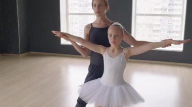 Stüdyoda klasik bale pozisyonunda dururken öğretmenin kızın el kaldırmasına yardım ettiği pozu kaldır.