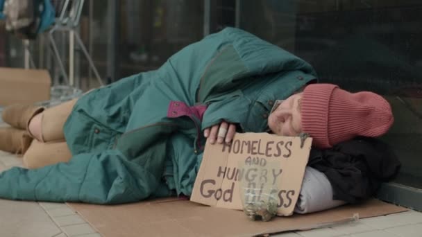 中等比例的露宿街头者穿着破布躺在标有 无家可归 标志的车上 乞求帮助 — 图库视频影像