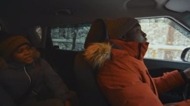 Afrika kökenli Amerikalı baba ve oğulun arabayla bir yere gidip ormanlık alandan geçerken konuşmalarının yan görüntüsü.
