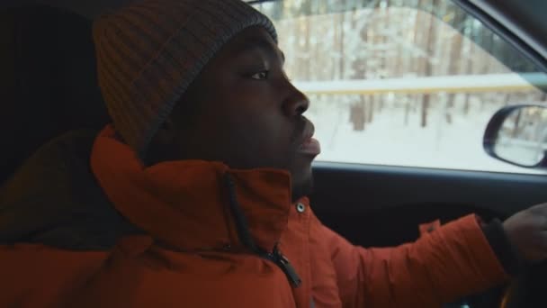 冬の間に暖かい服と帽子で車でどこかに行くアフリカ系アメリカ人の男性の中央閉鎖 窓の外の雪景色 — ストック動画