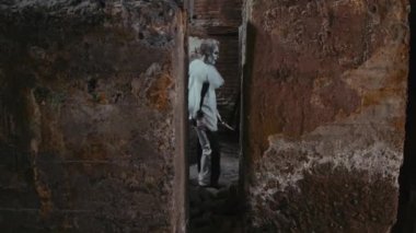 Bıçaklı korkunç palyaçonun duvardaki dar geçitten geçerek kameraya baktığı uzun bir çekim.