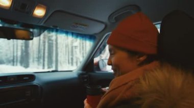 Şapkalı ve kalın elbiseli bir kadın yolcu koltuğunda oturuyor ve karlı ormana giderken biriyle konuşuyor.