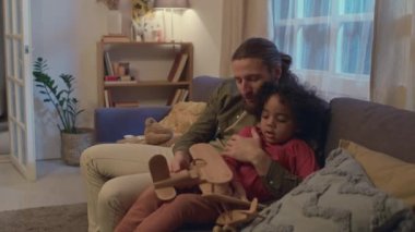 Çok ırklı baba ve oğul, rahat oturma odasındaki kanepede otururken tahta oyuncak uçakla oynuyorlar.