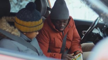 Afrika kökenli Amerikalı baba, kışın arabada otururken dijital tablet üzerinde oğlana yol tarifi yapıyor.