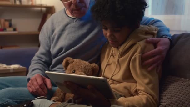 ソファーに座っているデジタルタブレットで祖父と孫が映画を観ている様子を撮影 — ストック動画