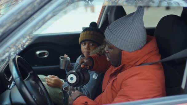 アフリカ系アメリカ人の家族 子供の側面から 冬の旅行中に車で休んでいる間に熱水瓶からお茶を飲む — ストック動画