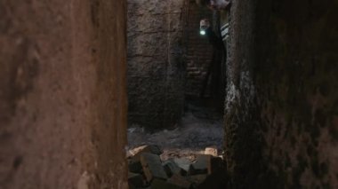 Yanlız başına terk edilmiş bir yeri keşfederken duvardaki dar geçitler arasında parlayan el fenerini yukarı kaldır.