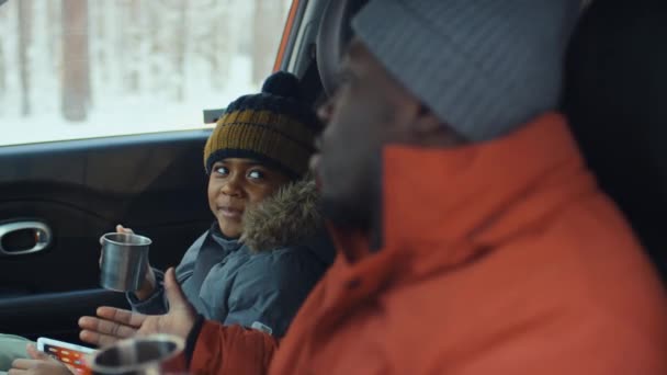 アフリカ系アメリカ人の父親と息子のラック フォーカスは 車に座り 旅行中に休んでいる間 テルモスからお茶を飲む — ストック動画