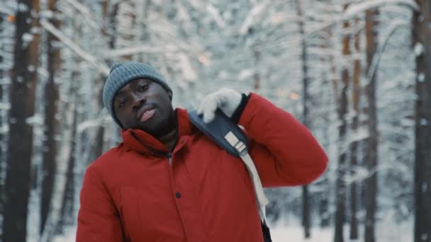 雪の森の景色に立ってカメラを見ている陽気な黒人男性のミディアム肖像画 — ストック動画