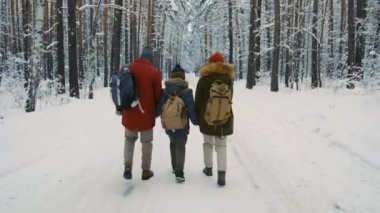 Üç kişilik ailenin bir arada el ele tutuşması ve karlı ağaçların arasında yolda yürümesi.