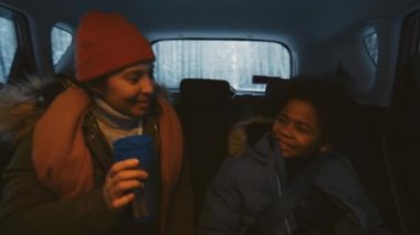 Kışın arabayla bir yere giderken, termo bardaklı bir kadının sıcak kıyafetler içinde oğlanla konuştuğu orta boy bir fotoğraf.