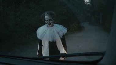 Orta boy palyaço kostümlü manyağın arabayı karanlık bir yerde yolda bırakarak hızla giderken görüntüsü.