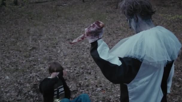 高角度的可怕小丑拿着刀冲向他的女受害者在黑暗的森林里向后爬去 — 图库视频影像