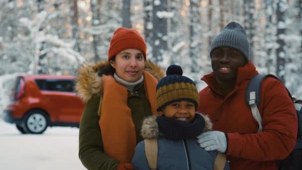 雪の森に立っている異文化の家族の肖像画 背景に赤い車とカメラを見る — ストック動画