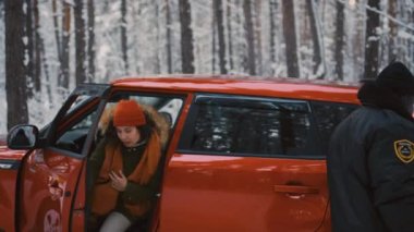 Afro-Amerikan trafik müfettişi kalın giysiler içinde kadın sürücüden karlı ormanda araba açmasını istiyor.