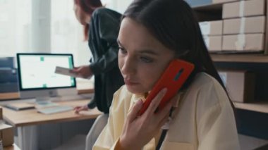 Başka bir işçi pazar yerinin deposunda kutu paketlerken, kadın yöneticinin müşterilerle cep telefonuyla konuştuğu orta ölçekli bir fotoğraf.