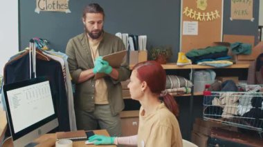 Ortalama bir bağış merkezi çalışanı ihtiyacı olan insanlar için nakliye kıyafetleri listesi hazırlıyor, konuşuyor ve bilgisayar başında oturuyor.