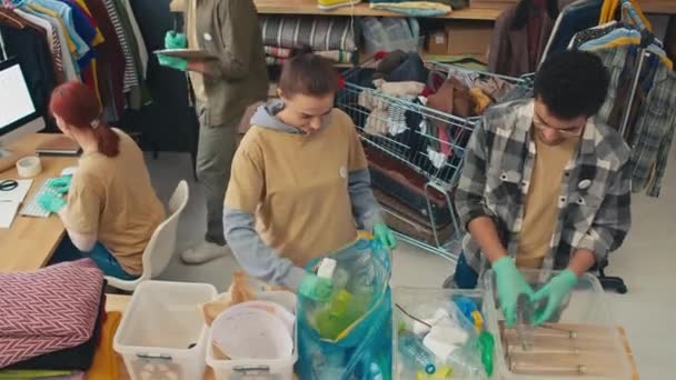 プラスチックボトルを容器に分類するチームの一部のハイアングルビュー 2番目の部分は貧しい人々のための人道援助として服を準備します — ストック動画