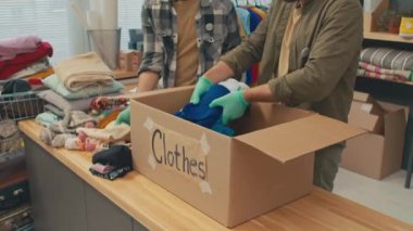 Bağış merkezinde çalışanların kesilen fotoğrafları, ihtiyaç sahiplerine yardım için paketleri hazırlarken giysileri kutuya koyuyorlar.