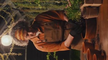 Kadın bahçıvanın serada çalışırken başka bir çömleğe çiçek naklettiği dikey çekim.