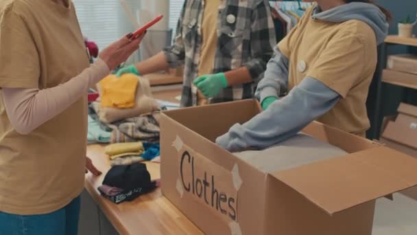 Średnie Ujęcie Małej Grupy Wolontariuszy Zbierających Ubrania Pudełku Dla Potrzebujących — Wideo stockowe