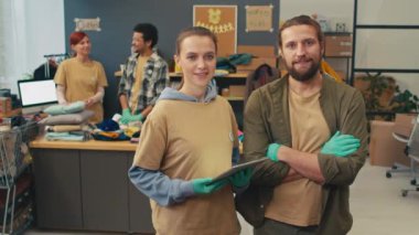 Erkek ve kadın bağış merkezi gönüllülerinin portresi kameraya bakarken, diğerleri ihtiyacı olan insanlar için ikinci el eşyalar sıralıyor.