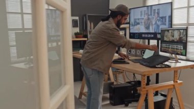 Genç Arap erkek tasarımcının eve gelip dizüstü bilgisayarı açması ve profesyonel video düzenleme yazılımında çalışmaya devam etmesi.