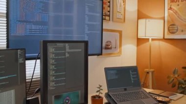 Evde çalışan programcının ya da IT çalışanının orta ekran görüntüsü, kodlu büyük bilgisayar ekranları, dizüstü bilgisayar, not defteri, klavye ve kahve kupası.
