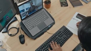 Erkek geliştiricinin klavyeye bilgisayar kodu yazıp not defterine yazarken, iş arkadaşıyla dizüstü bilgisayarda görüntülü konuşma yaparken en iyi görüntüsü