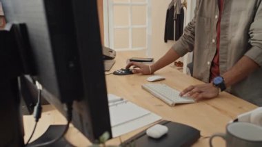 Evdeki çalışma masasında duran, klavye ve multimedya kontrol faresini kullanarak bilgisayardaki ham görüntüleri düzenleyen tanınmayan bir erkek grafik tasarımcısının orta boy el ve vücut görüntüsü.