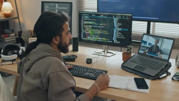 男性软件开发人员坐在办公桌前 有几个电脑屏幕 一边和同事在笔记本电脑上视频交谈 一边讨论问题和争论 一边在家里工作 — 图库视频影像