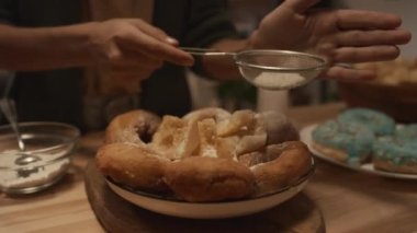 Kimliği belirsiz genç bir kızın ellerinin yakın plan çekimi donut tozu ve pudra şekerli börekler içerken aynı zamanda elek aile kutlamasına hazırlanıyor.